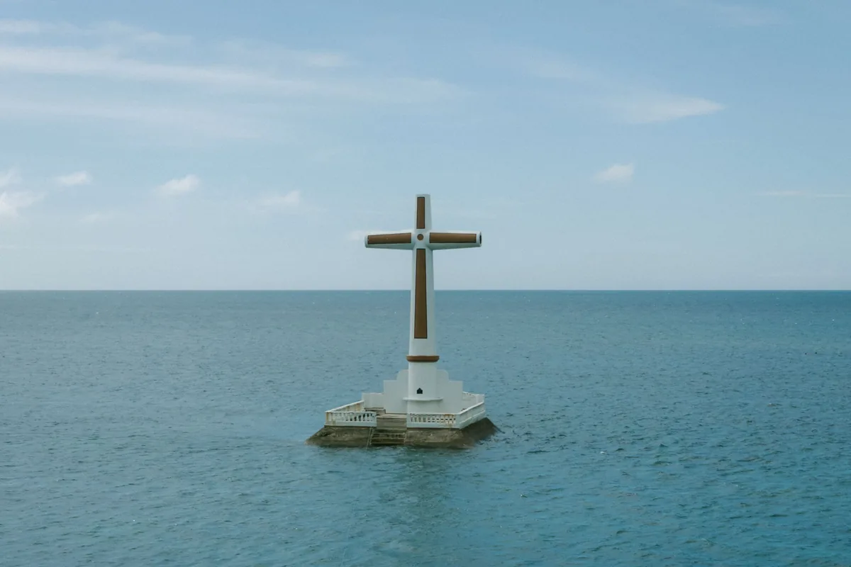 The white marker cross of the Sunken Cemetery standing in calm blue sea off Camiguin, Philippines
